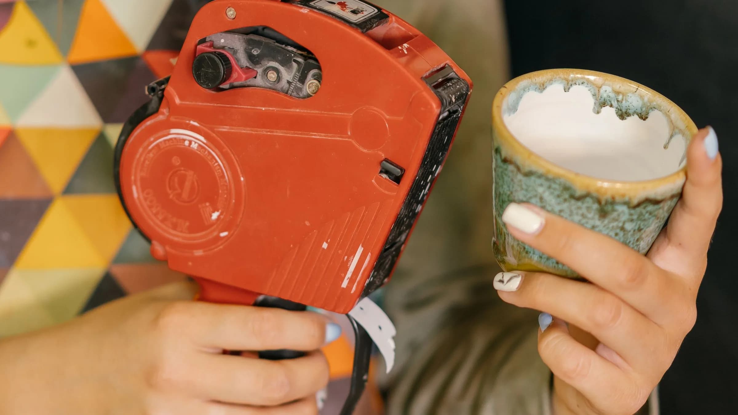 A shop worker holds a price-tag gun in one hand and a handmade ceramic cup in the other.